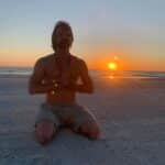 Man meditating on a beech at sunset